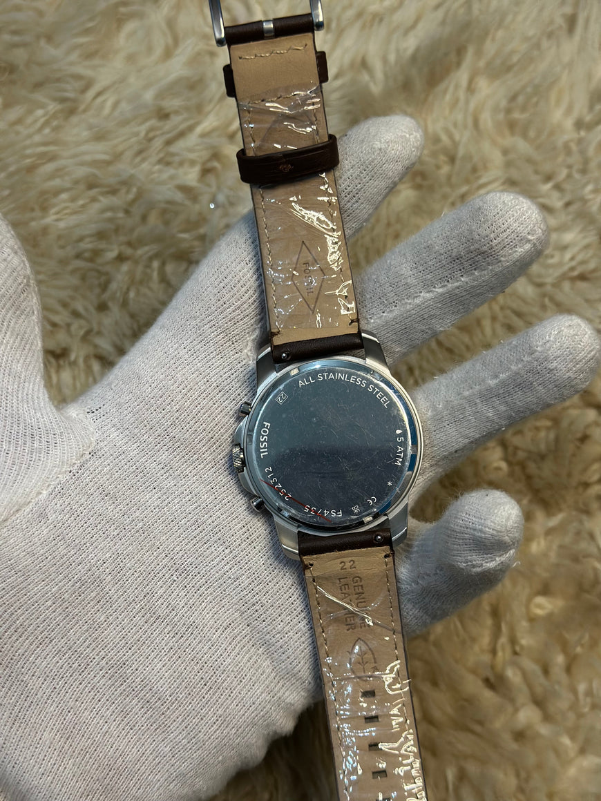 Watch with a textured strap on a hand wearing a gray glove against a beige background